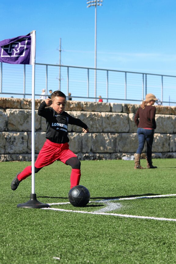 Child kicking soccer ball on field